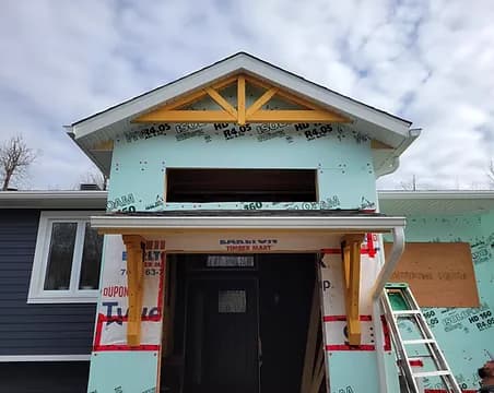 A house under construction showing exterior sheathing, insulation and a cedar entry portico being framed